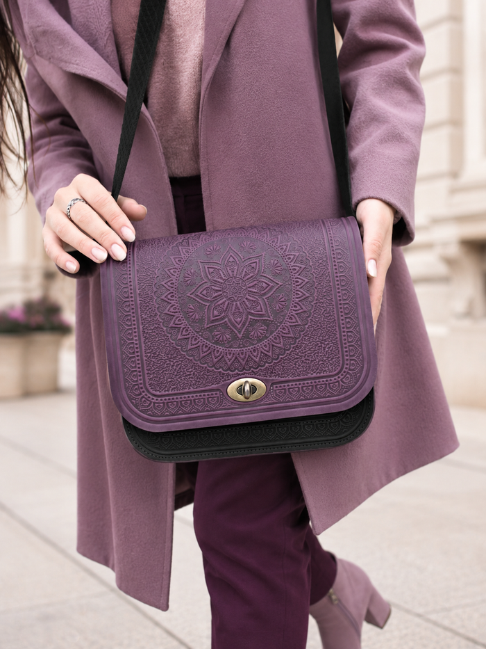 A person wearing a mauve coat and matching pants carries a mauve embossed flap shoulder bag with a black strap and black bottom trim, shown outdoors on a sidewalk.