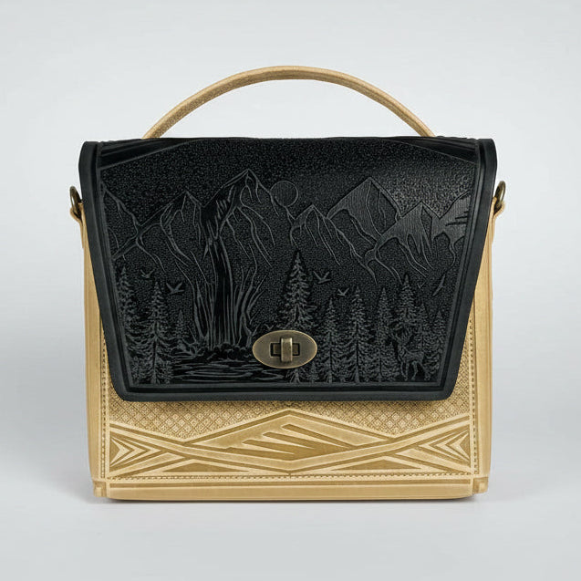 Handbag with black and gold design against a white brick wall.