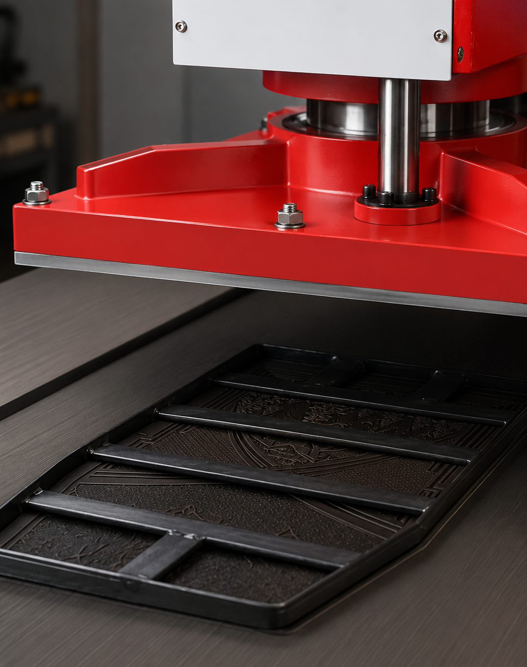 A close-up of a press leather cutting machine lowering onto a black rectangular tray with embossed decorative patterns, set on a dark gray tabletop.