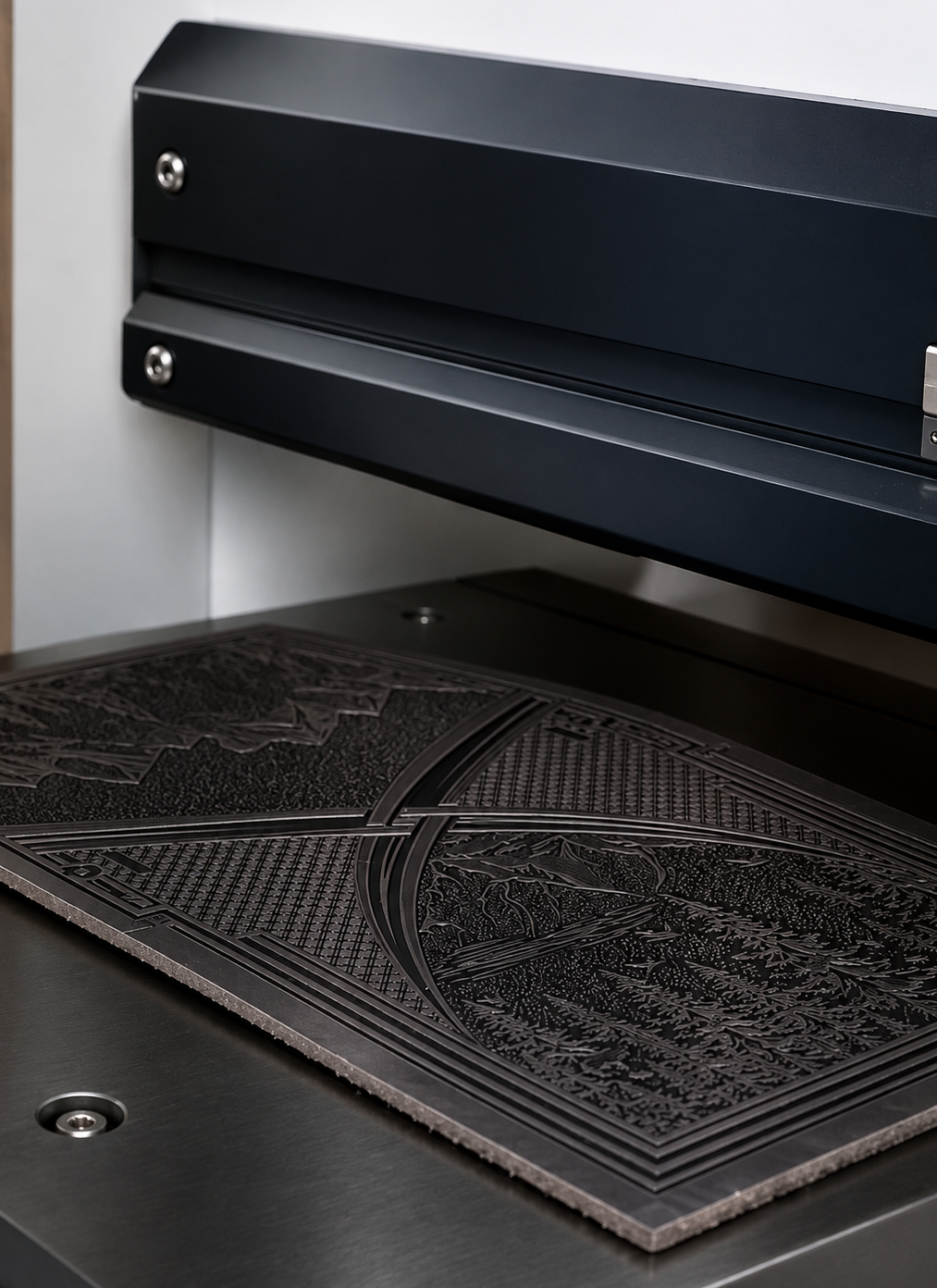 A close-up of a heat-stamping machine with an embossed geometric and floral pattern, positioned on a dark metal work surface under a black machine arm.